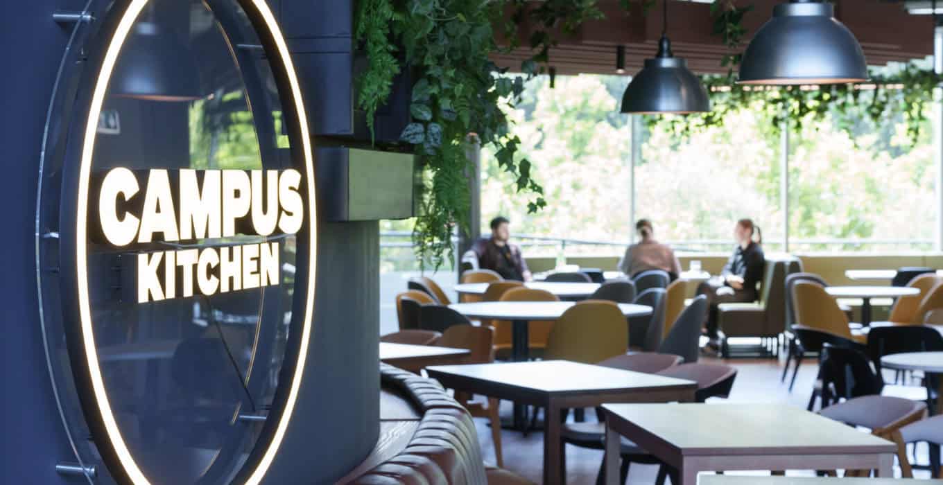 A campus cafeteria with a sign on the wall saying "Campus Kitchen".