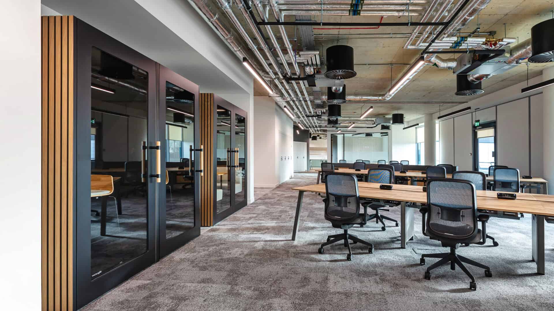 A modern office space with a long table, black chairs, and large windows.